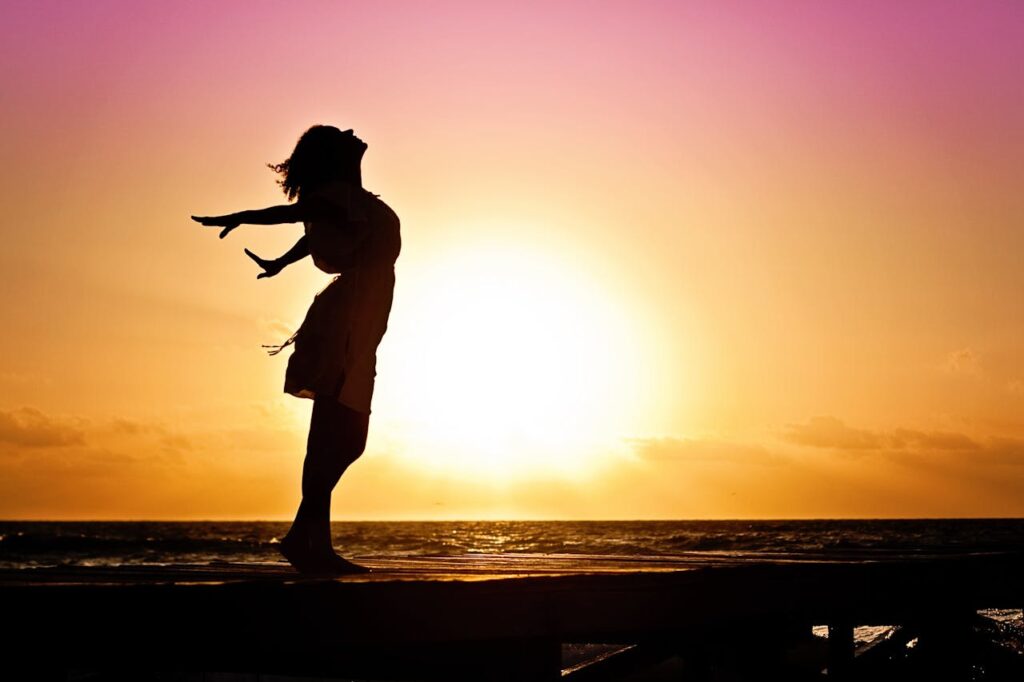woman happiness sunrise silhouette 40192 Silhouette of a woman at the beach with arms outstretched against a vibrant sunset backdrop.